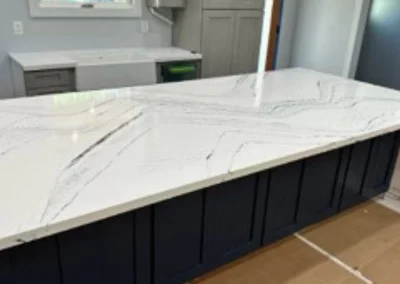 Modern kitchen with a large white countertop featuring dark veining, paired with navy blue cabinetry and a light-filled space.
